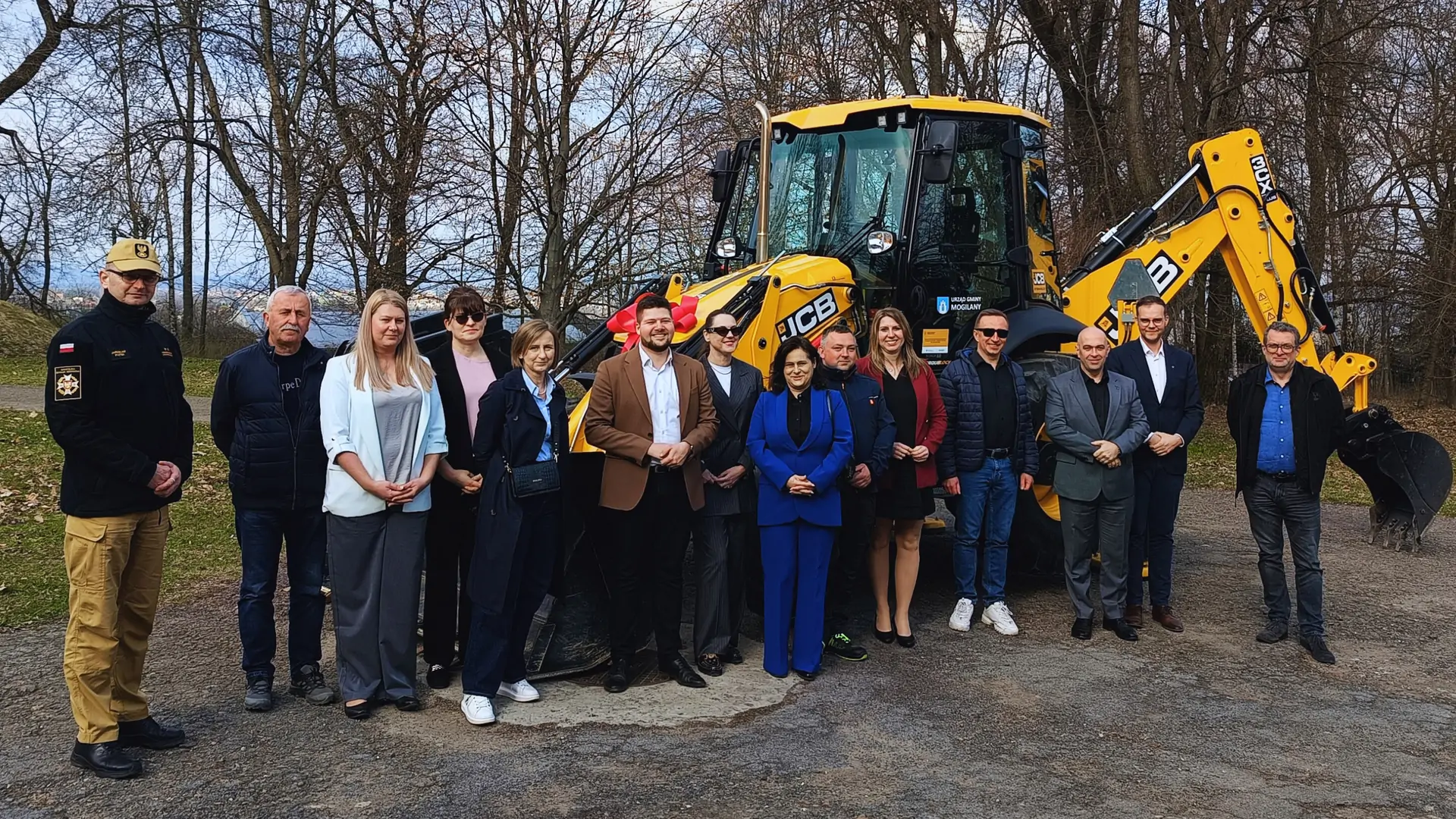 Zdjęcie grupowe. Osoby stoją na tle nowo zakupionej koparki.
